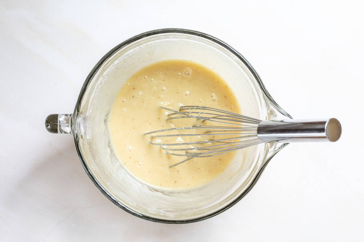 Financier batter in mixing bowl with whisk.
