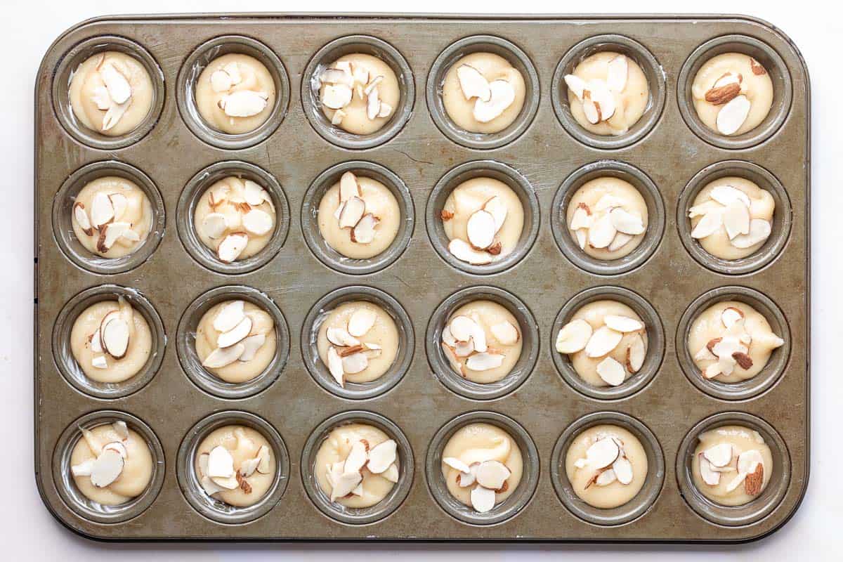 Muffin tin with almond financier batter topped with sliced almonds.