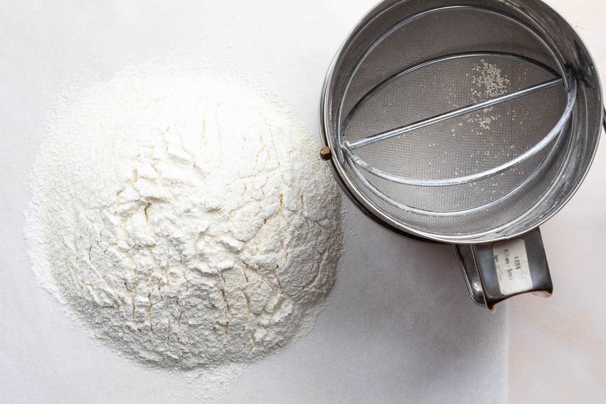 sifted almond flour, regular flour, and powdered sugar on parchment next to sifter.