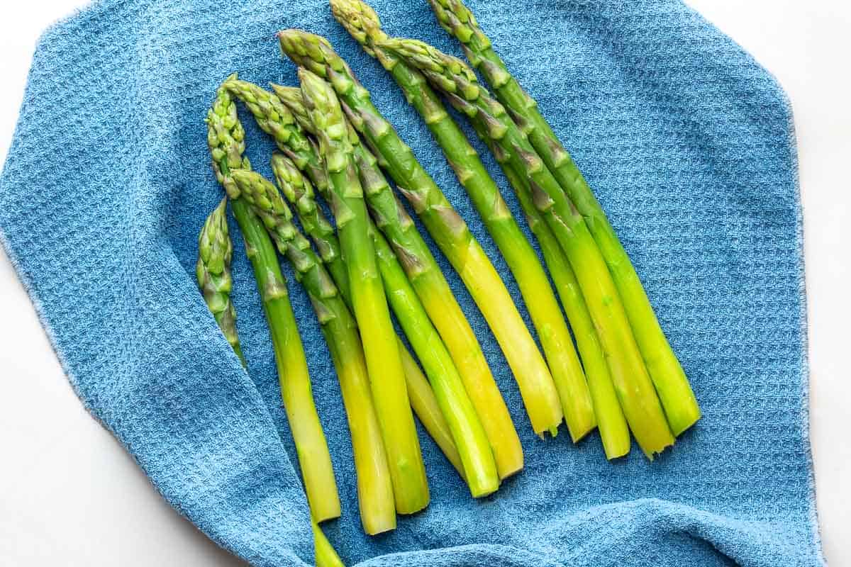 Several stalks of steamed asparagus are drying on a textured blue towel.