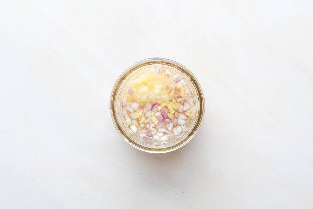 Overhead view of jar with lemon juice, orange juice, dijon mustard, and chopped shallots.