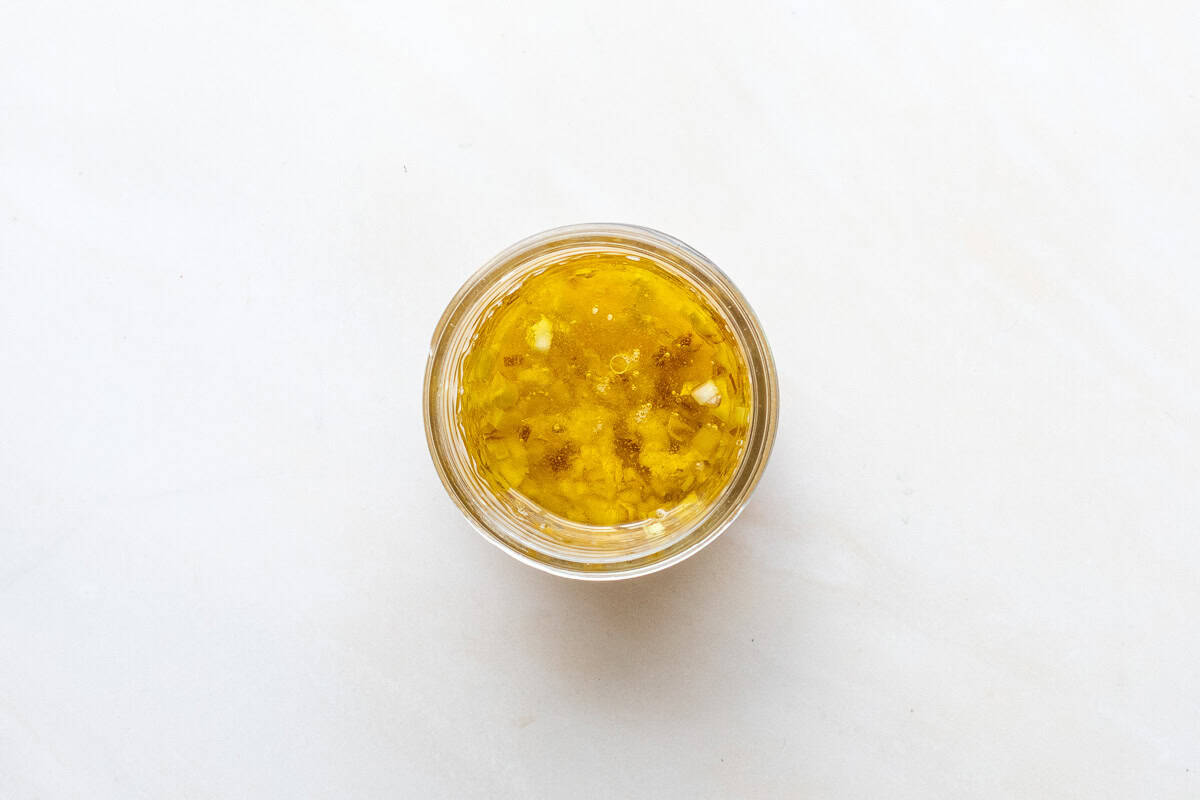 A small glass jar filled with unmixed citrus vinaigrette viewed from above on a light surface.