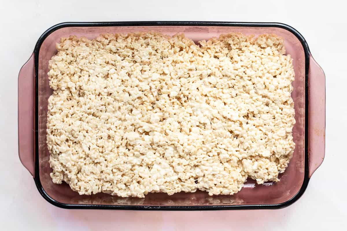 A glass baking dish filled with a layer of homemade brown butter Rice Krispies treats, shown from above on a white surface.
