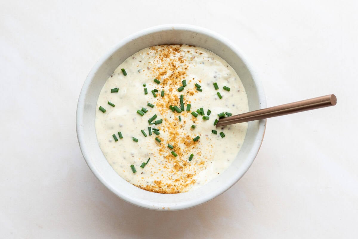 Bowl of creamy sauce for crab cakes topped with chopped chives and Old Bay seasoning.