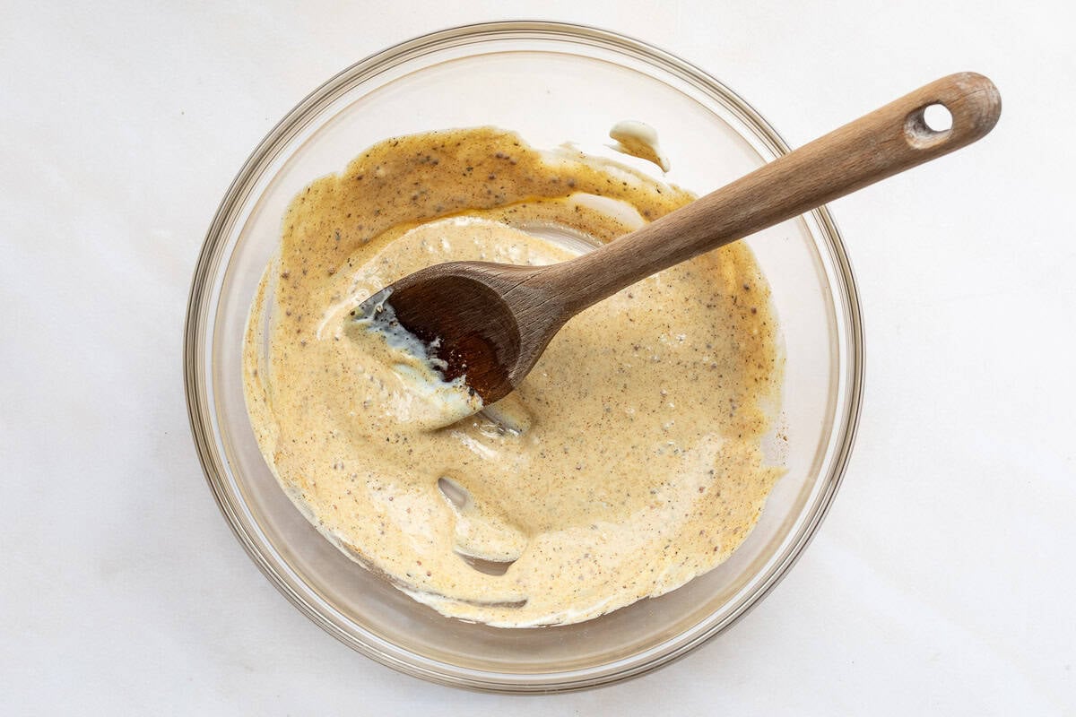 Binding sauce for crab balls in a large mixing bowl with a wooden spoon.