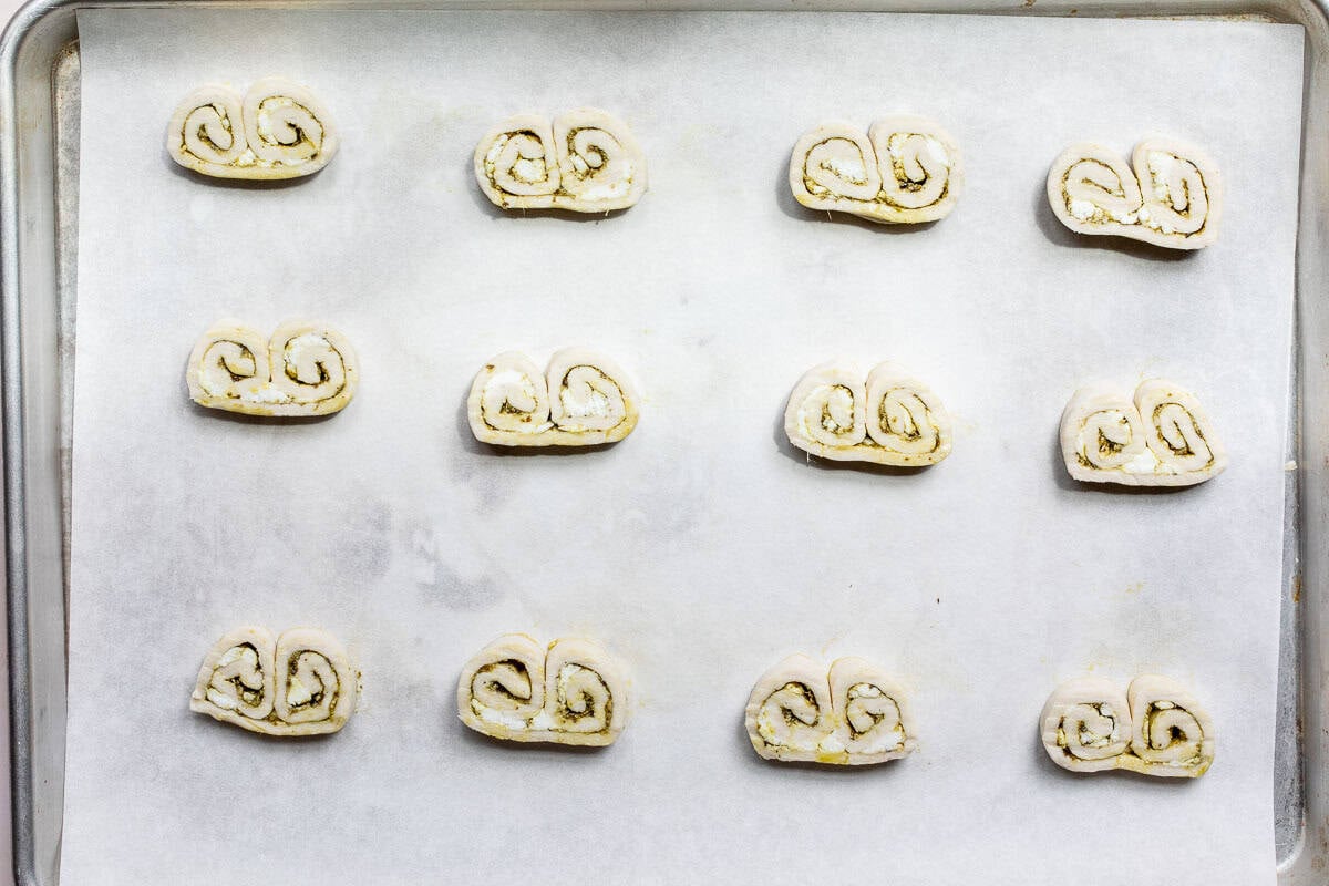 Twelve unbaked savory palmiers arranged evenly on a parchment-lined baking sheet, ready to be baked.