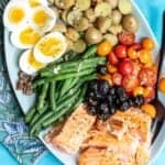A platter of Salmon Niçoise salad with salmon, hard-boiled eggs, roasted potatoes, green beans, olives, and halved cherry tomatoes.